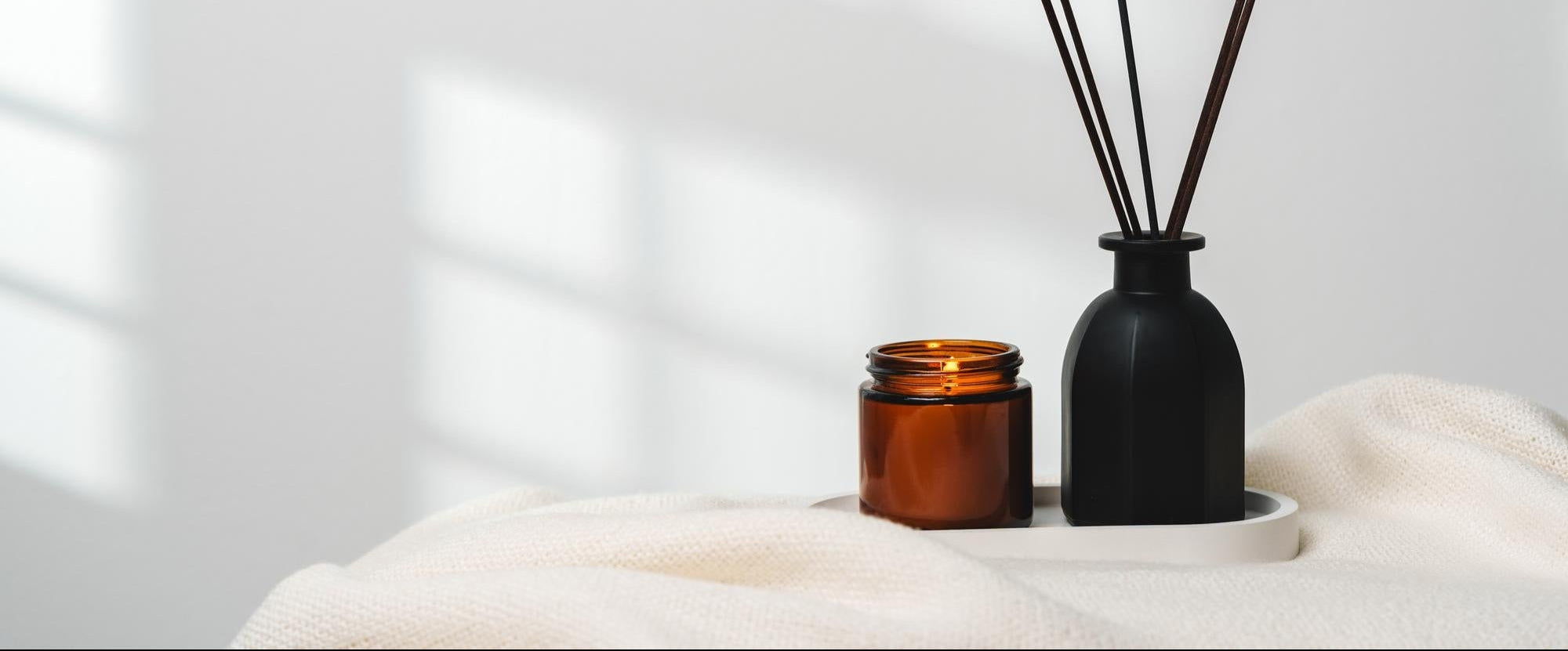 Elegant aroma diffuser with reed sticks and scented candle on white tablecloth