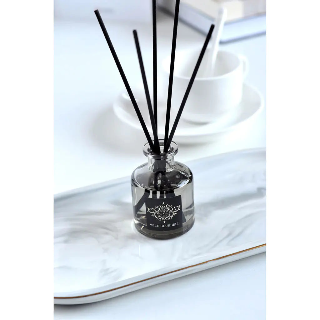 Reed diffuser with black sticks in a clear bottle on a marble surface